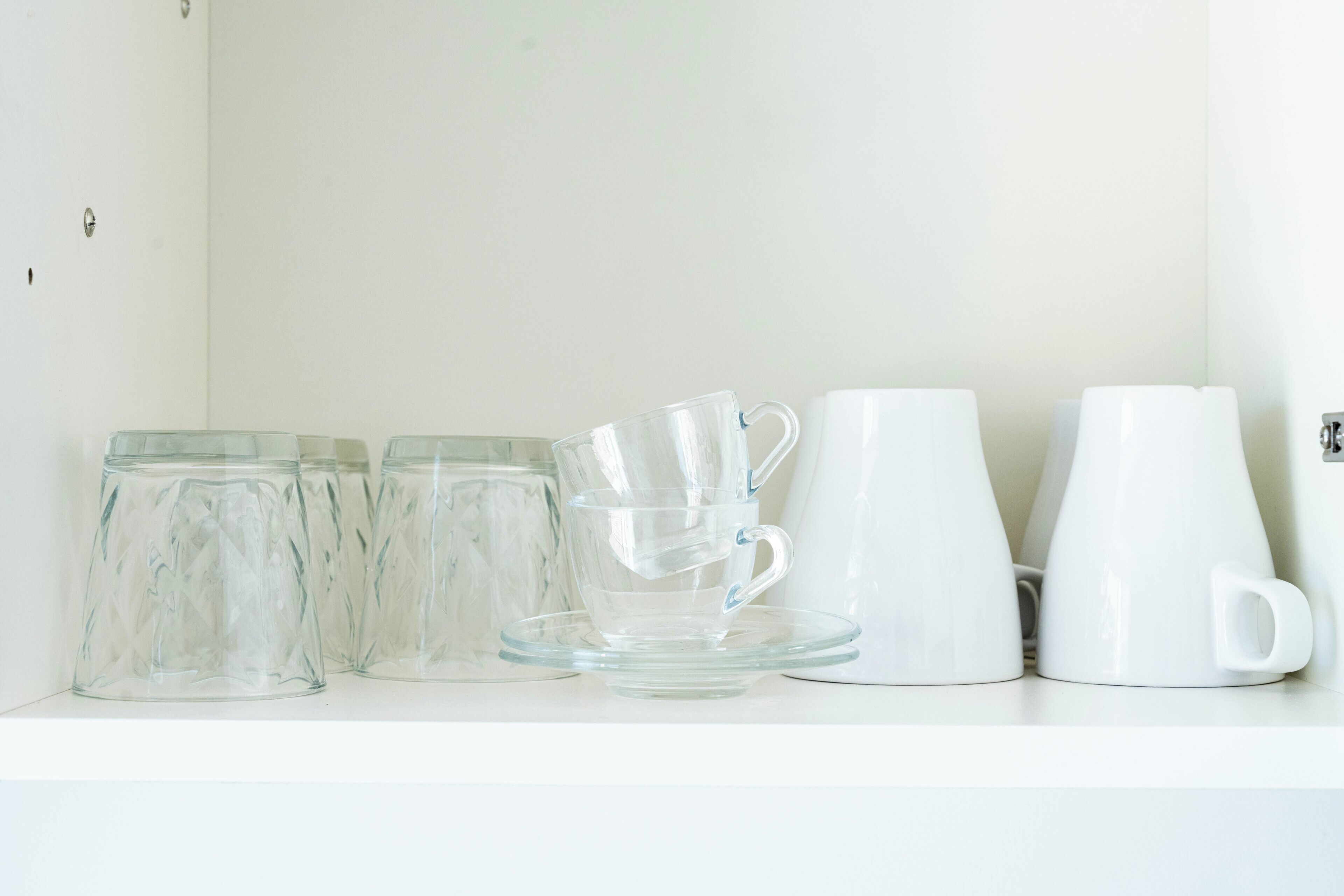 A white shelf with clear glass cups, a glass mug, and a white pitcher.