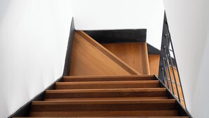 Een trap met houten treden en een metalen leuning, die uitkomt op een vloer van hout.