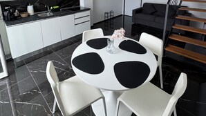 Een moderne keuken met witte kasten, een zwart aanrecht en een eethoek met een ronde tafel en witte stoelen.