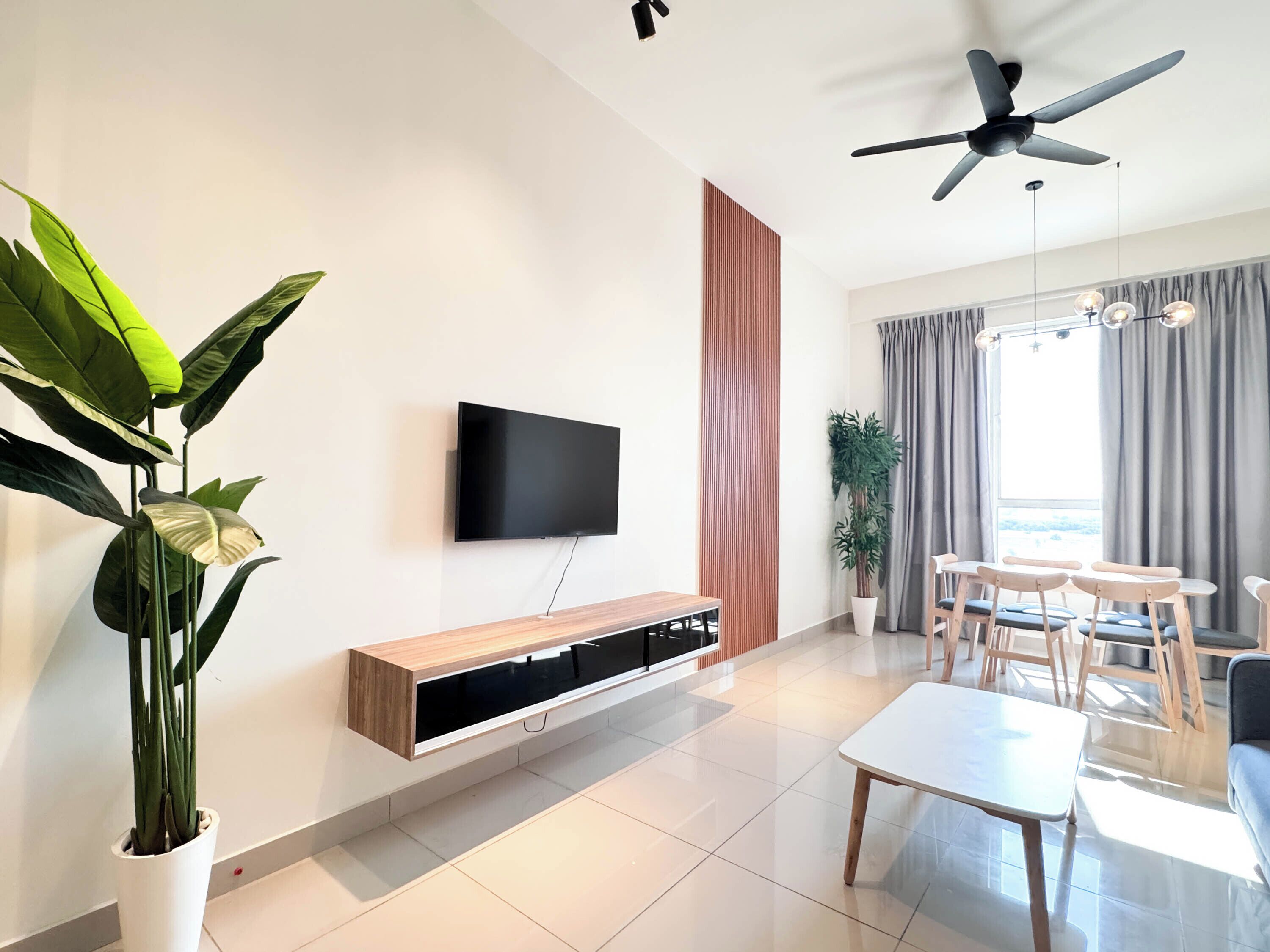 Uma sala de estar moderna com televisão de tela plana, ventilador de teto, área de jantar com mesa e cadeiras, e uma grande planta em vaso.
