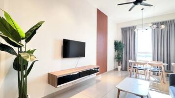 Uma sala de estar moderna com televisão de tela plana, ventilador de teto, área de jantar com mesa e cadeiras, e uma grande planta em vaso.