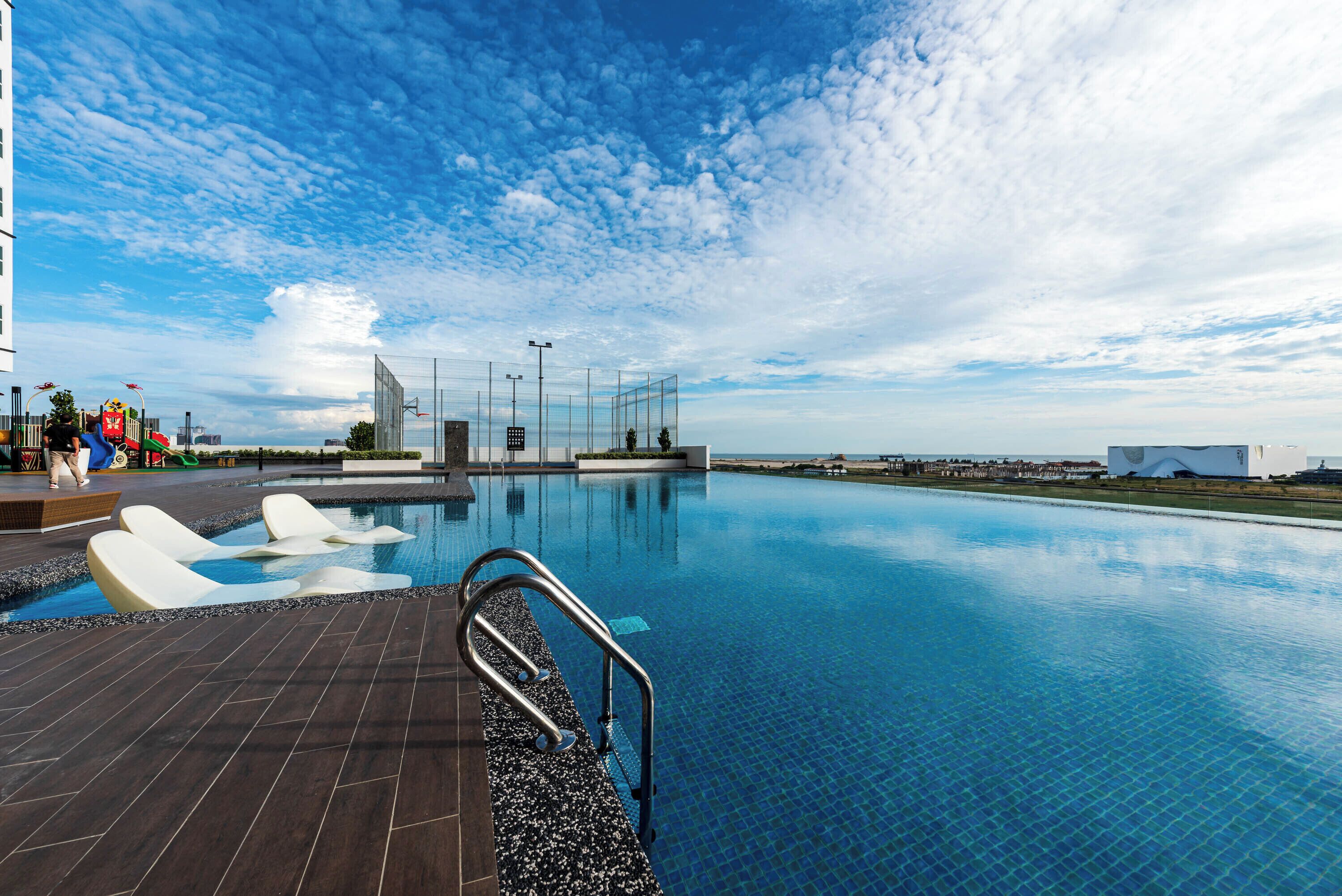 A swimming pool with a tiled deck, a metal handrail, and a clear blue sky.