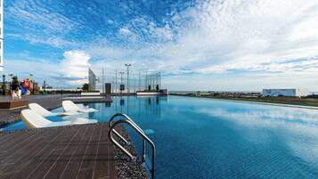 A swimming pool with a tiled deck, a metal handrail, and a clear blue sky.