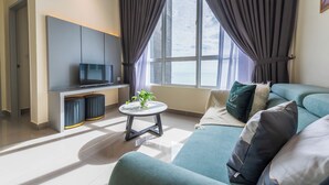 Una sala de estar moderna con un sofá, un televisor, una mesita con una planta y una ventana con cortinas.