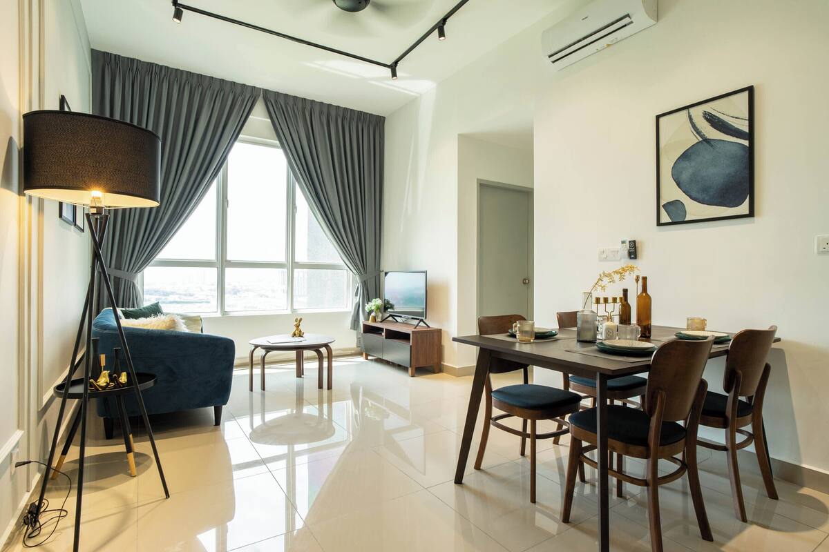 A modern living room with a sofa, dining table, chairs, a lamp, a TV, and a painting on the wall.