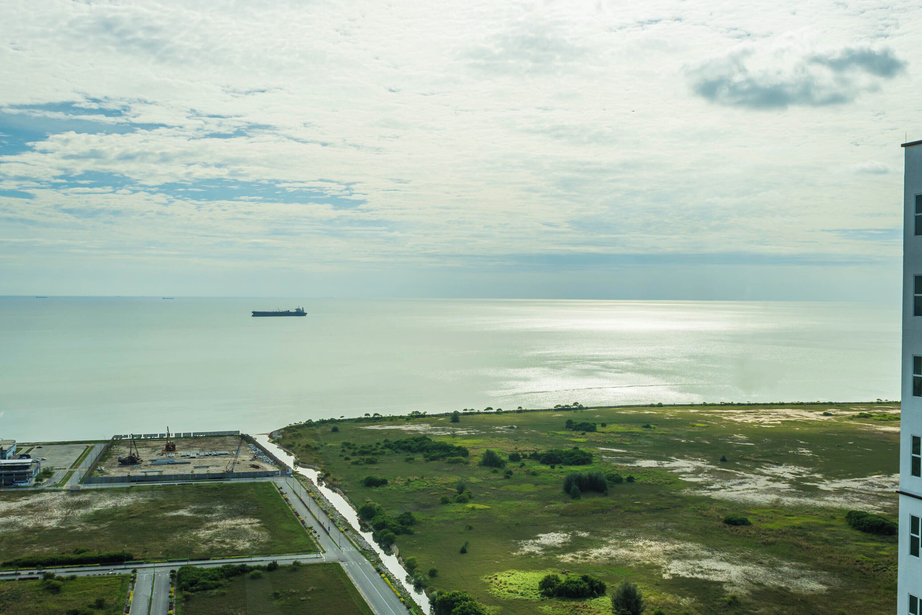A coastal landscape with a ship in the distance, a road, and a building on the right.