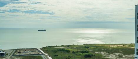 A coastal landscape with a ship in the distance, a road, and a building on the right.