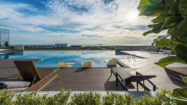 Un área de piscina en la azotea con sillones, piscina y cielo despejado.