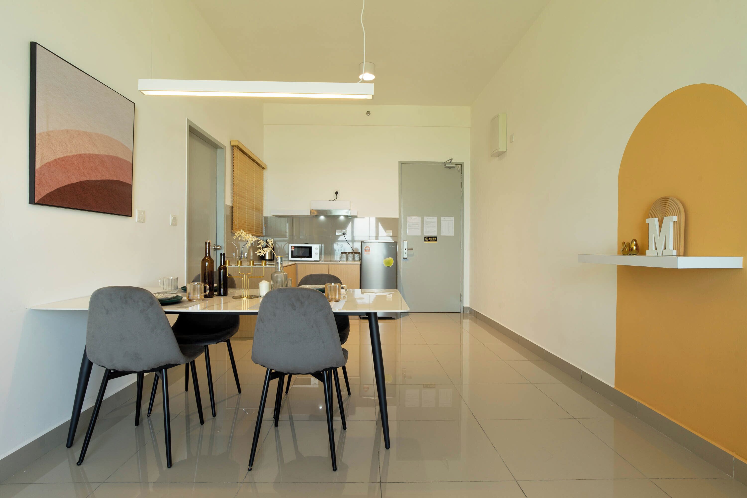 A modern kitchen with a microwave, oven, and refrigerator, a dining area with a table and chairs, and a hallway leading to a bedroom.