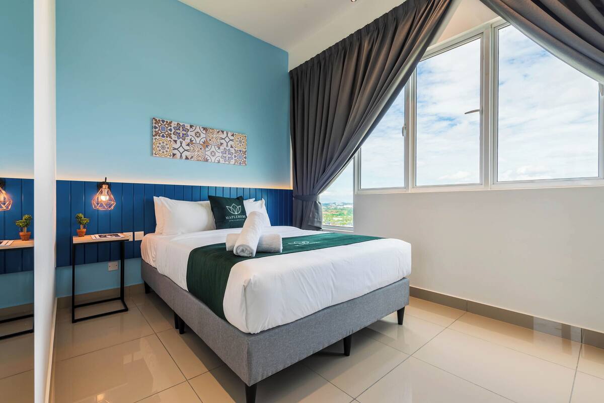A hotel room with a bed, a nightstand, a wall-mounted artwork, and a window with curtains.