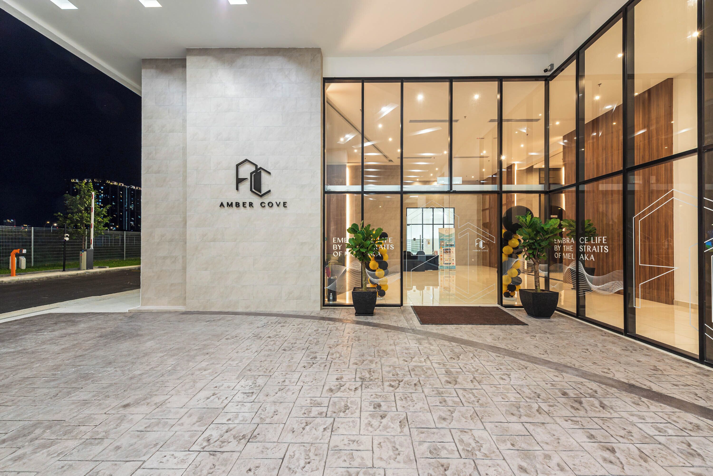 A modern hotel entrance with a glass facade, a logo on the wall, and potted plants.
