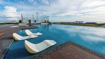 A swimming pool with lounge chairs, a wooden deck, and a view of the sea.