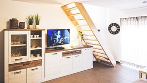 Een woonkamer met een televisie, een houten trap en een kast met glazen deuren.