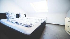 Een slaapkamer met een bed, een dressoir, een dakraam en een betegelde vloer.