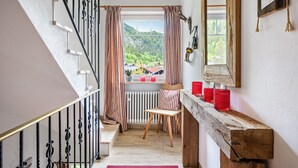 Una escala amb barana de fusta, una cadira, una finestra amb cortines i una prestatgeria amb contenidors vermells.