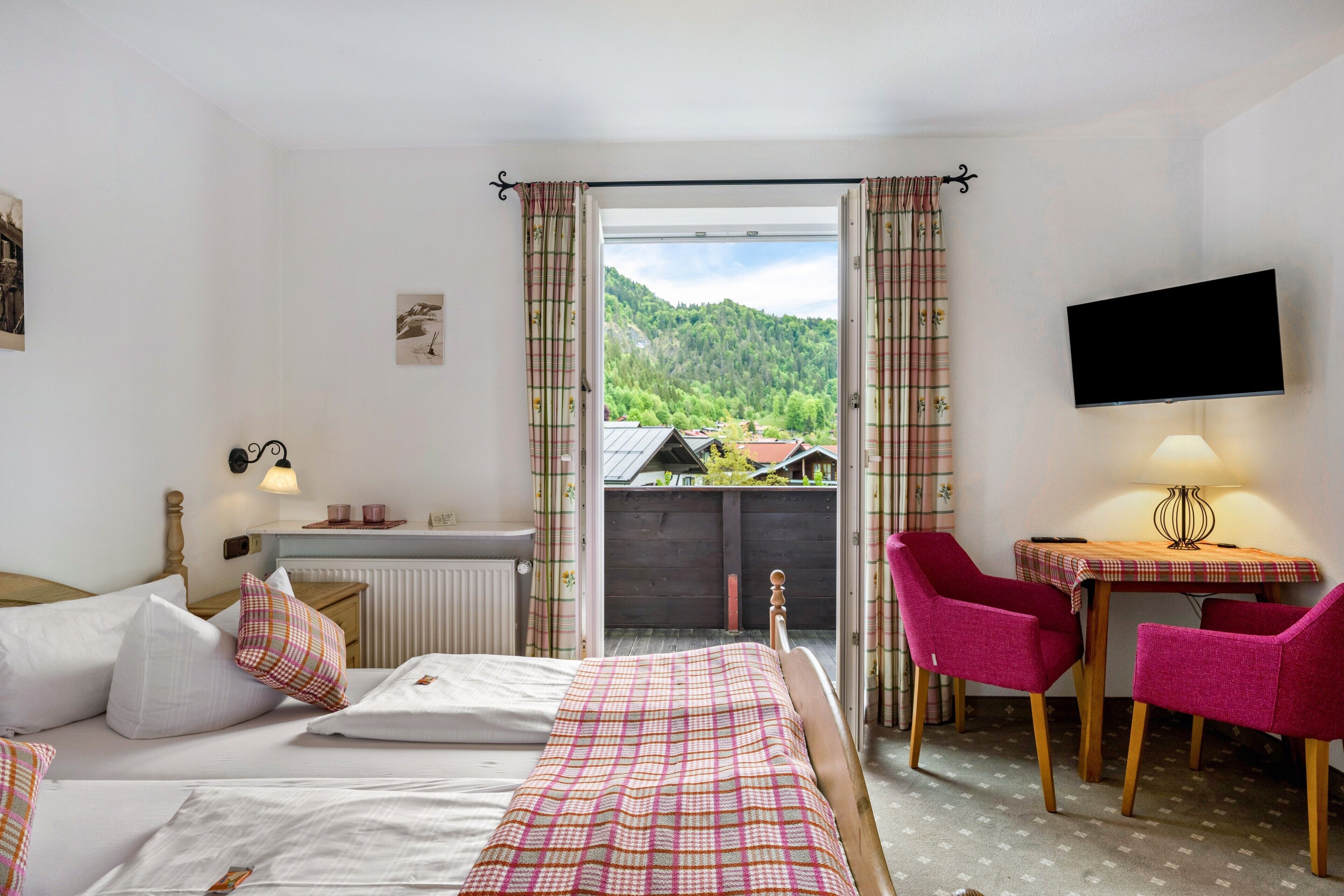 A hotel room with a bed, a table with chairs, a TV, and a view of a mountain.