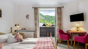 A hotel room with a bed, a table with chairs, a TV, and a view of a mountain.