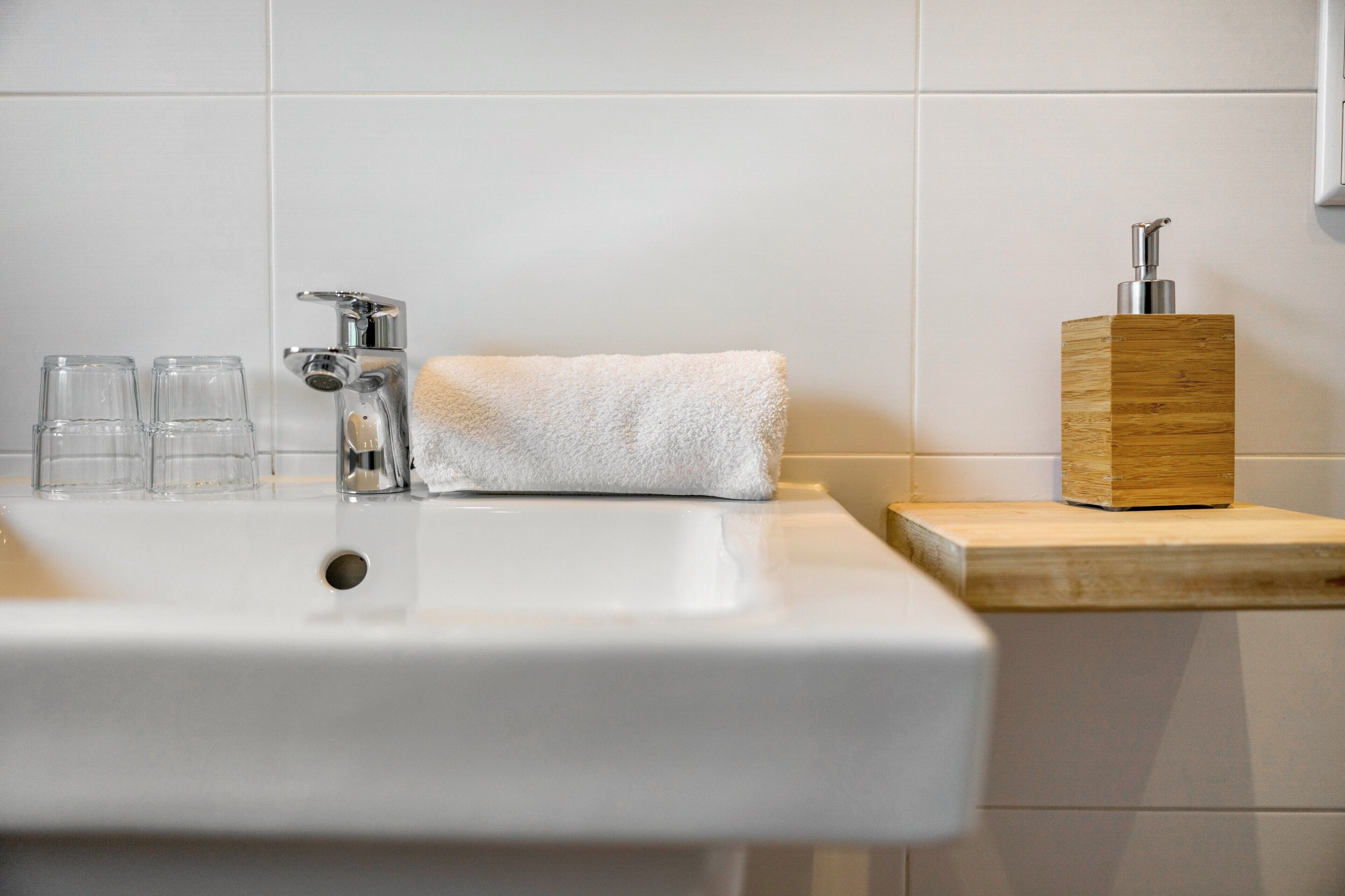 Un lavabo de salle de bain avec un robinet, une serviette blanche et un distributeur de savon, le tout posé sur une étagère en bois.