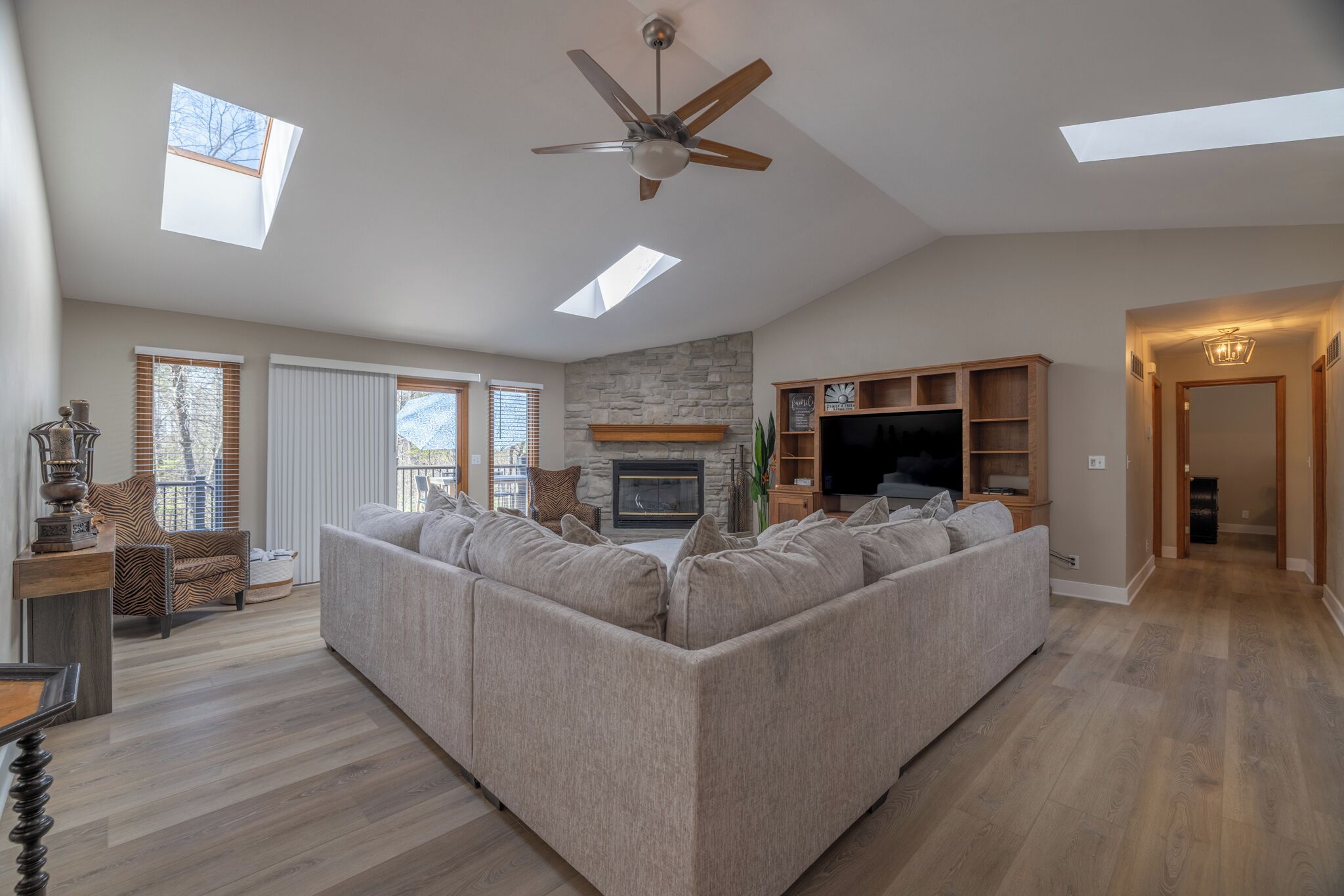 A spacious living room with a sectional sofa, a fireplace, a ceiling fan, and a TV.