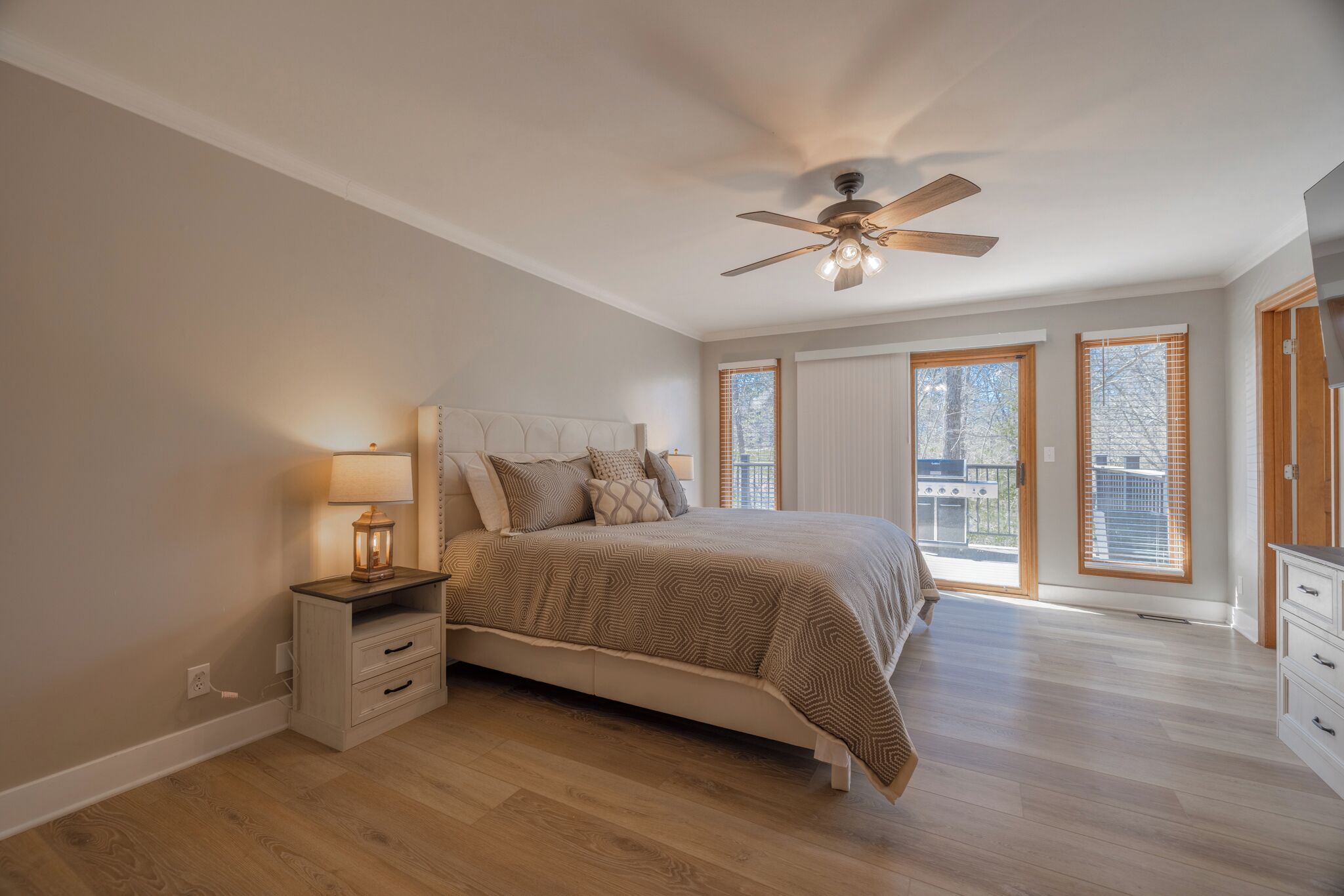 A bedroom with a bed, a nightstand, a ceiling fan, and large windows.
