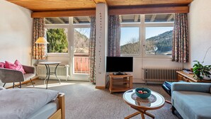 Una habitación con cama, sofá, televisión, una mesita y ventana con cortinas.