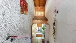 Una escalera estrecha con barandilla roja, techo de madera y vistas a una habitación con una puerta al final.