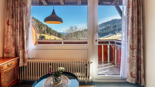 Habitación con vistas a un paisaje montañoso, techo de madera, radiador y una mesa con un florero.