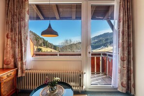 Ein Zimmer mit Blick auf eine gebirgige Landschaft, einer Holzbalkendecke, einem Heizkörper und einem Tisch mit einer Vase.