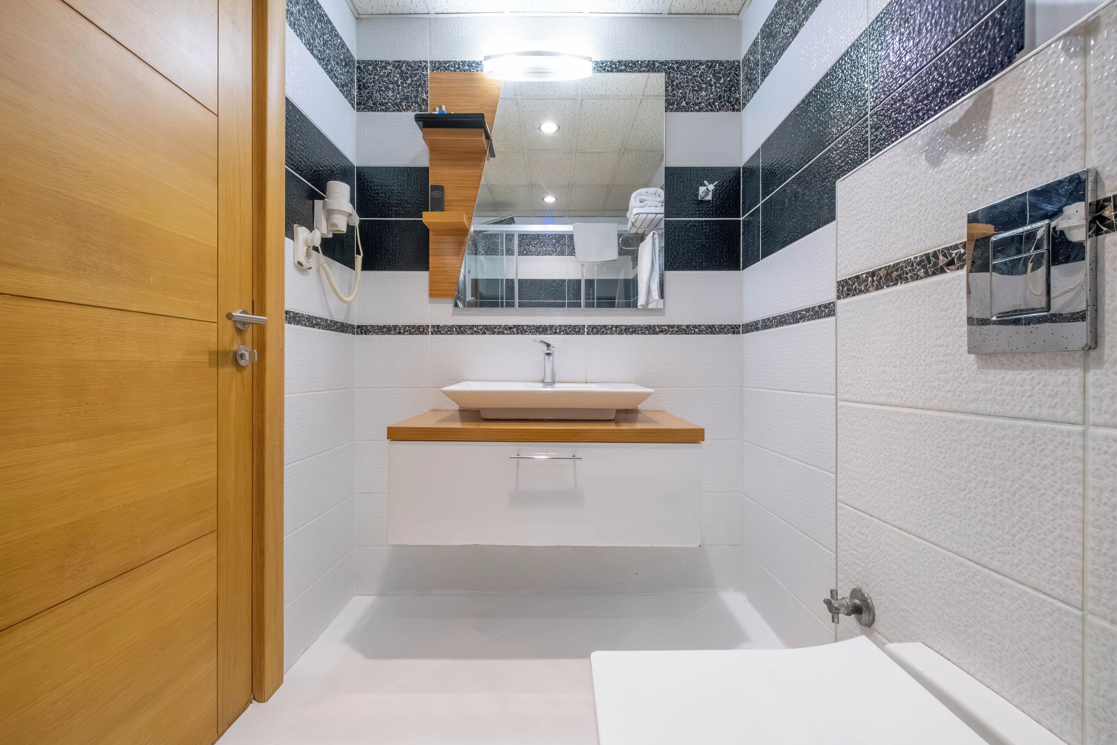 A bathroom with a wooden door, a sink with a mirror above it, and a shower area.