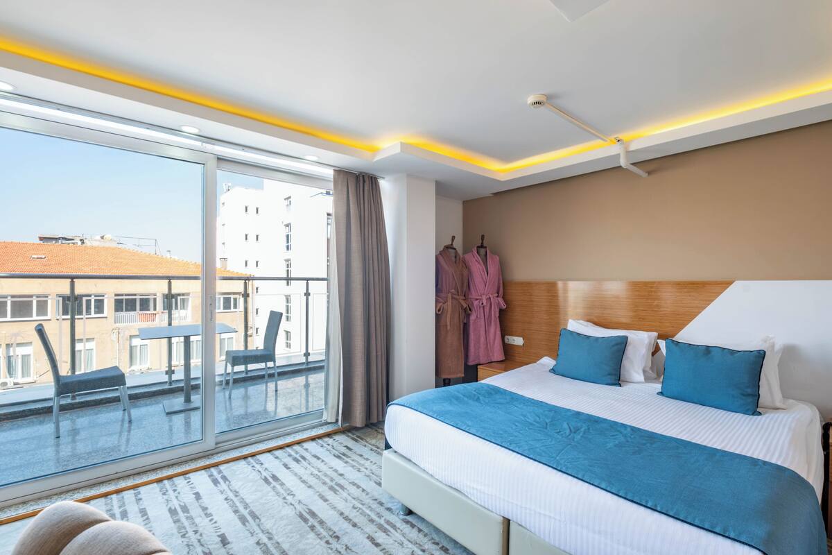 A hotel room with a large bed, a balcony with chairs, and a view of buildings.