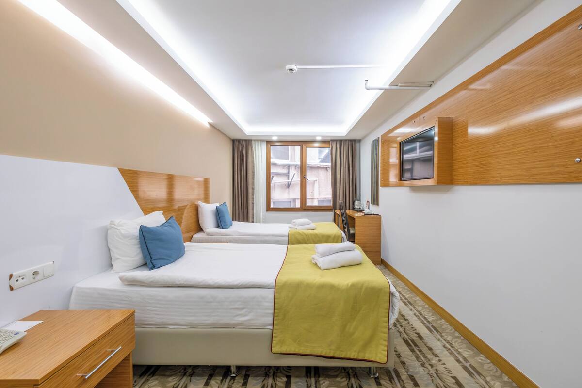 A hotel room with two beds, a desk, a TV, and a window with curtains.