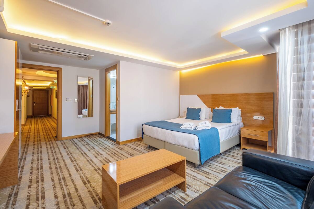 A hotel room with a bed, a sofa, a coffee table, a bedside table, and a mirror.