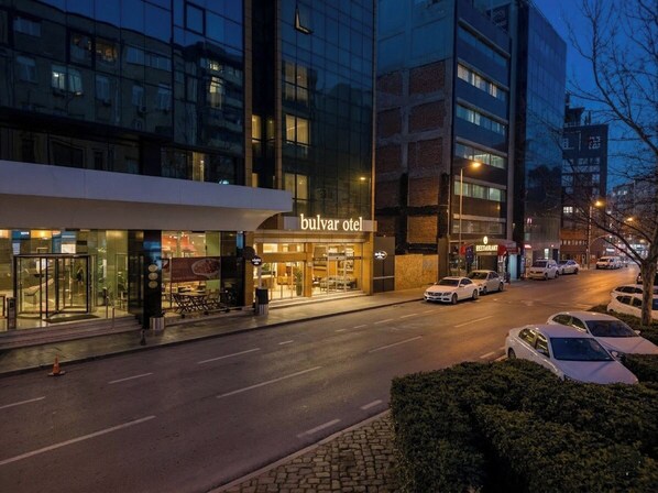 A hotel named 'bulvar otel' with a glass facade, a visible entrance, and parked cars along the street. - Bulvar Hotel (Izmir)
