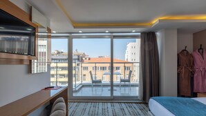 Habitación de hotel con cama, escritorio, silla, televisor y vistas a edificios a través de amplias ventanas.