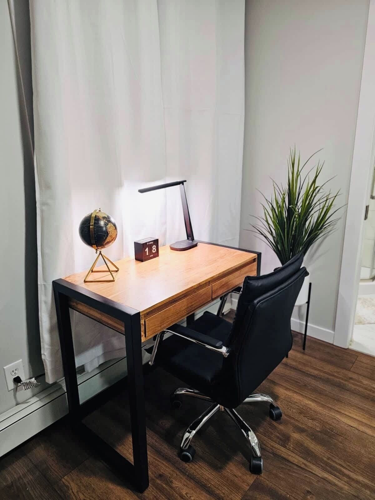 A wooden desk with a black office chair, a desk lamp, a small globe, and a clock.