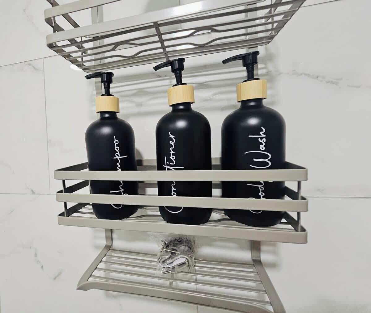 Une étagère de salle de bain avec trois bouteilles noires étiquetées « shampoing », « après-shampoing » et « gel douche ».