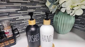 A kitchen counter with two soap dispensers labeled 'DISHES' and 'HANDS,' a green vase with white flowers, and a black container with a jar.