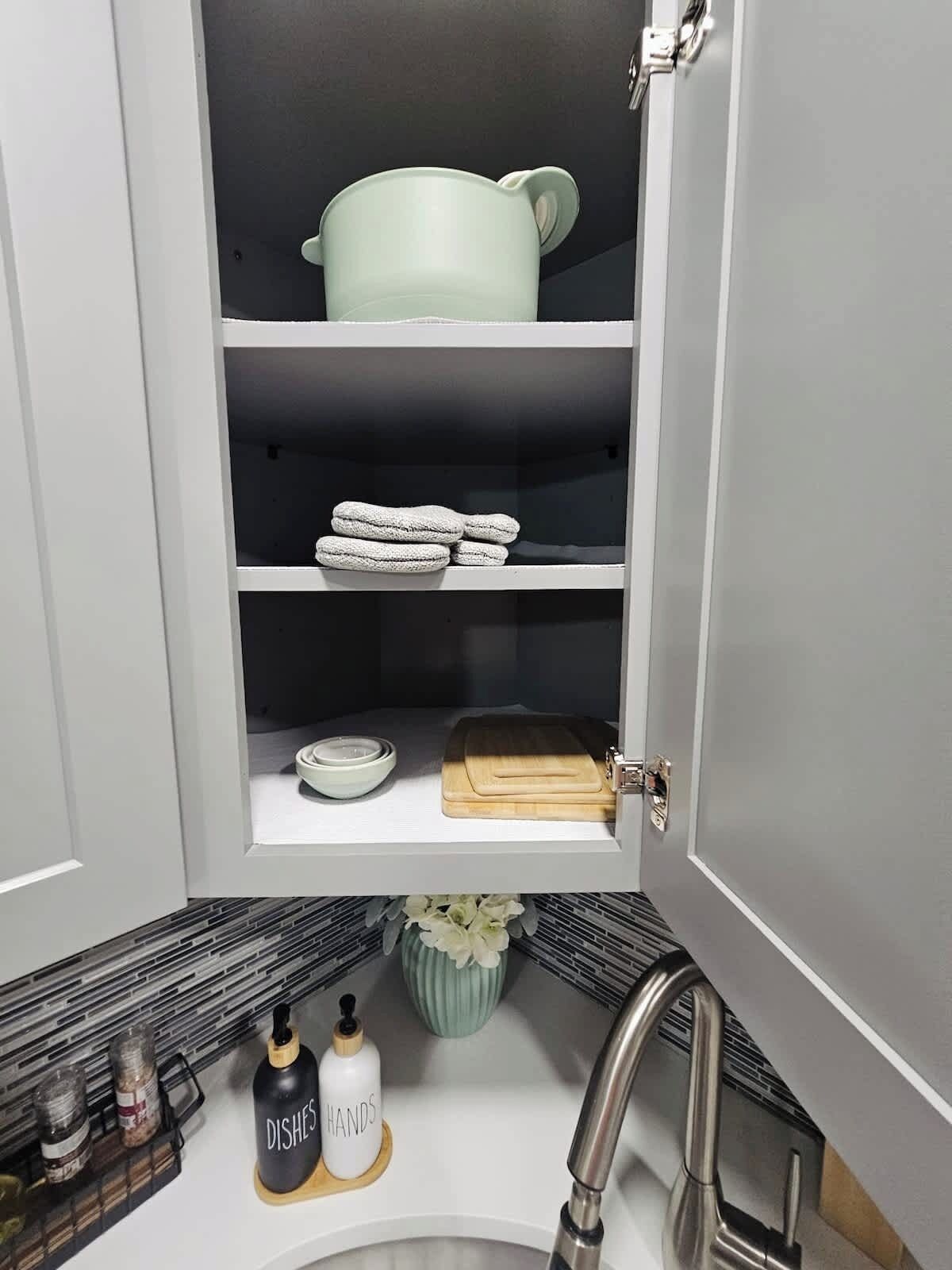 A kitchen with a white cabinet, a sink, and a countertop with a cutting board and a bowl.