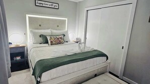 Une chambre à coucher comprenant un lit, des tables de chevet, un banc, une lampe fixée au mur et une porte.