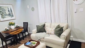Un salon avec un canapé beige, une petite table sur laquelle se trouve un plateau, un fauteuil et un tableau encadré accroché au mur.