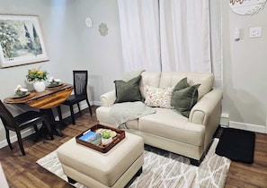 Una sala de estar con un sofá color beige, una mesita con bandeja, una silla y un cuadro en la pared.
