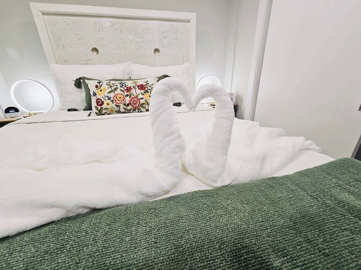 Una cama con ropa blanca, un plaid verde y una almohada estampada.