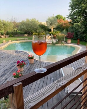 Eine Holzterrasse mit einem Glas rotem Getränk, einem Pool und Topfpflanzen.
