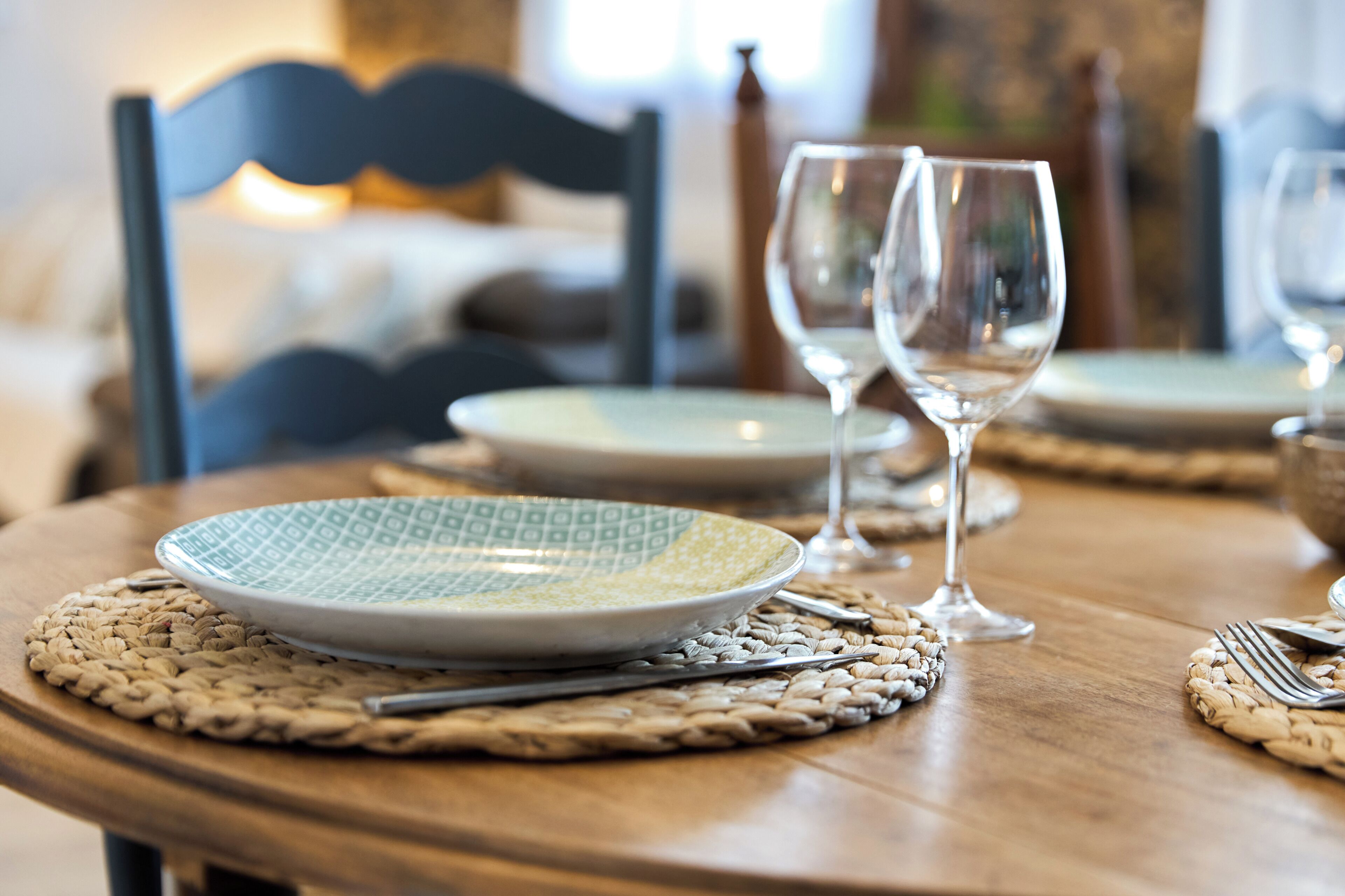 A dining table with a plate, cutlery, and two wine glasses set on a woven placemat.