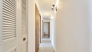 Un pasillo con una puerta, un accesorio de luz en la pared y un papel tapiz al final.