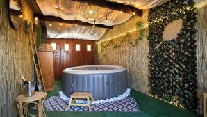 Una bañera de hidromasaje en una habitación con paredes de bambú, una puerta de madera y un pequeño taburete de madera.