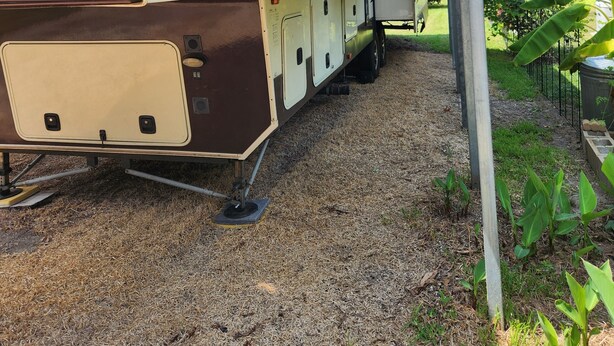 A recreational vehicle parked under a shelter with a covered bed area and a small attached kitchen space. - Beautiful 5th wheel with 4 slides in point blank (Point Blank)