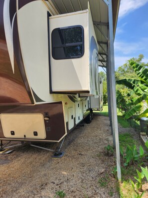 A recreational vehicle parked under a shelter with a covered bed area and a small attached kitchen space.