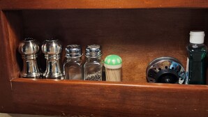 A wooden shelf with various kitchen items including salt and pepper shakers, a bottle of dish soap, and a metal container.