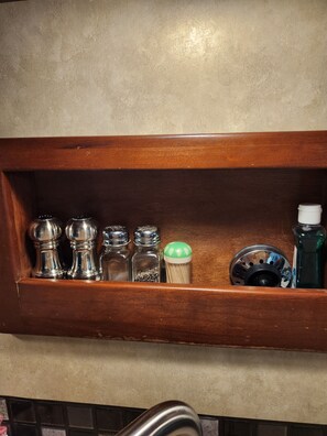 A wooden shelf with various kitchen items including salt and pepper shakers, a bottle of dish soap, and a metal container.
